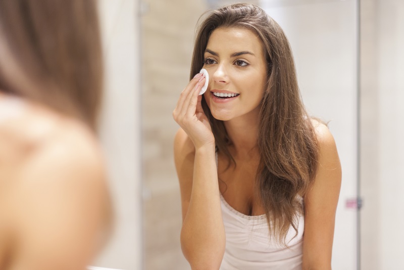 Mulher jovem em frente ao espelho tirando maquiagem do rosto antes de dormir